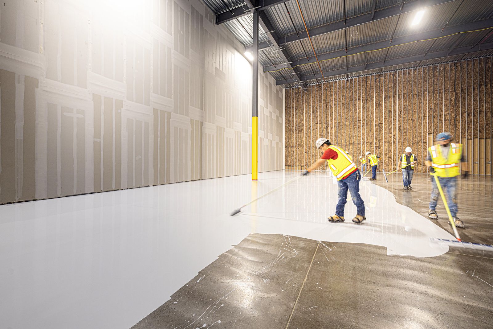 Crew spreading a fresh floor coating across a warehouse slab